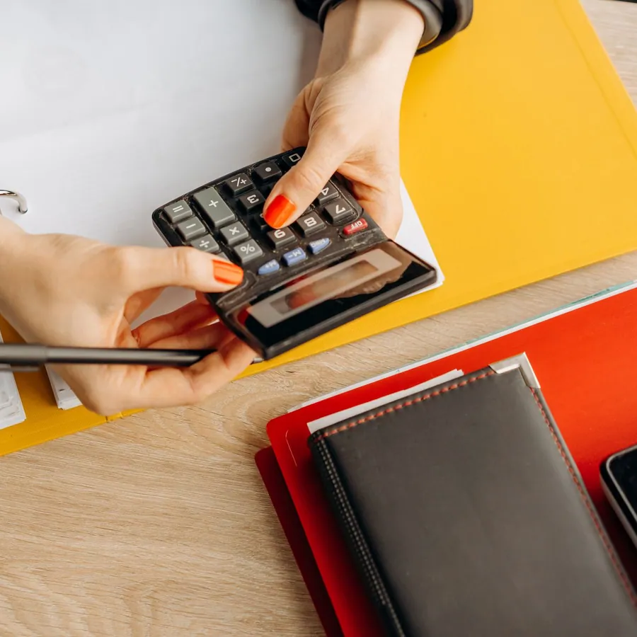 Mãos usando calculadora sobre uma mesa com documentos e pastas